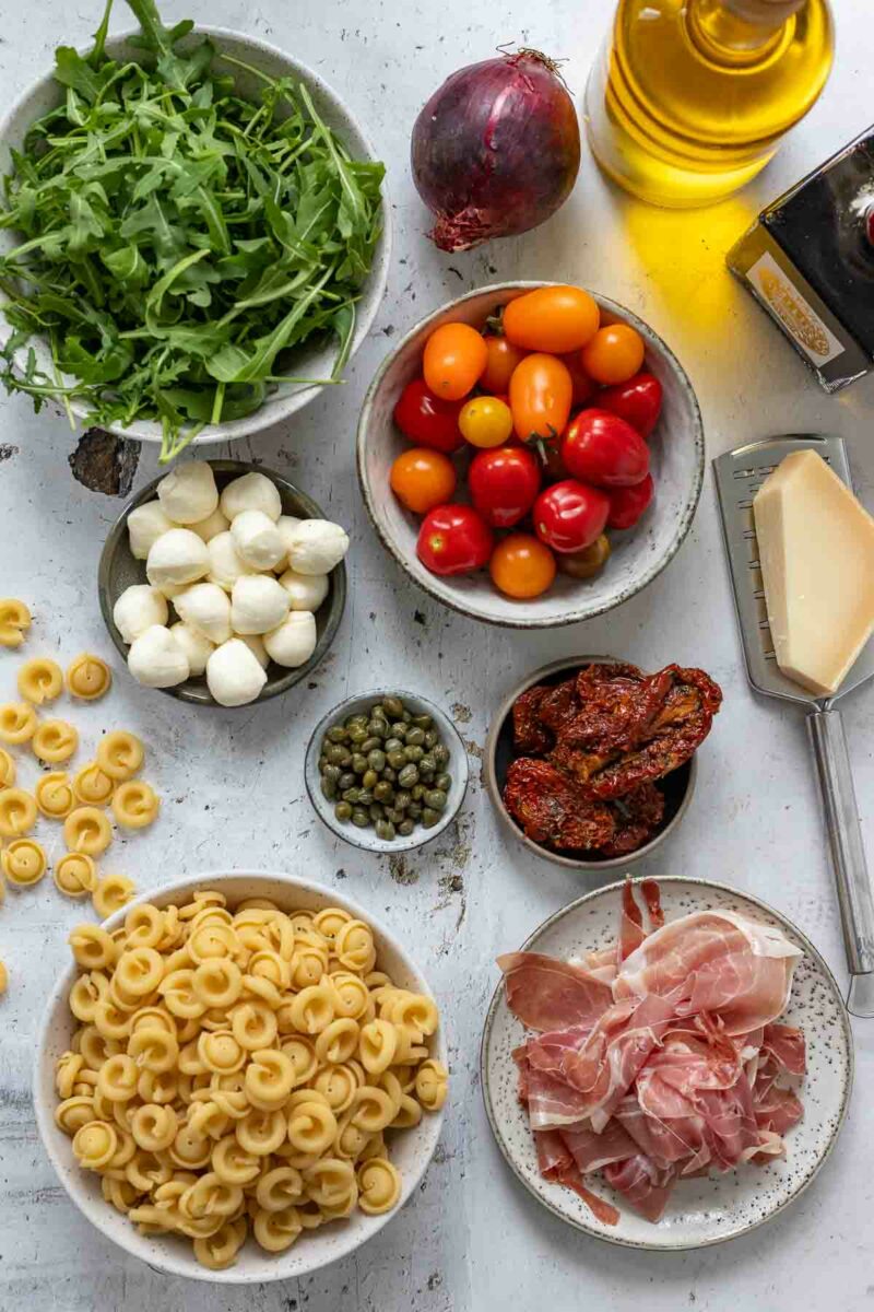 Zutaten für mediterraner Pastasalat mit Vollkornnudeln, Parmaschinken, Mini‑Mozzarella, Kapern und frischen Tomaten