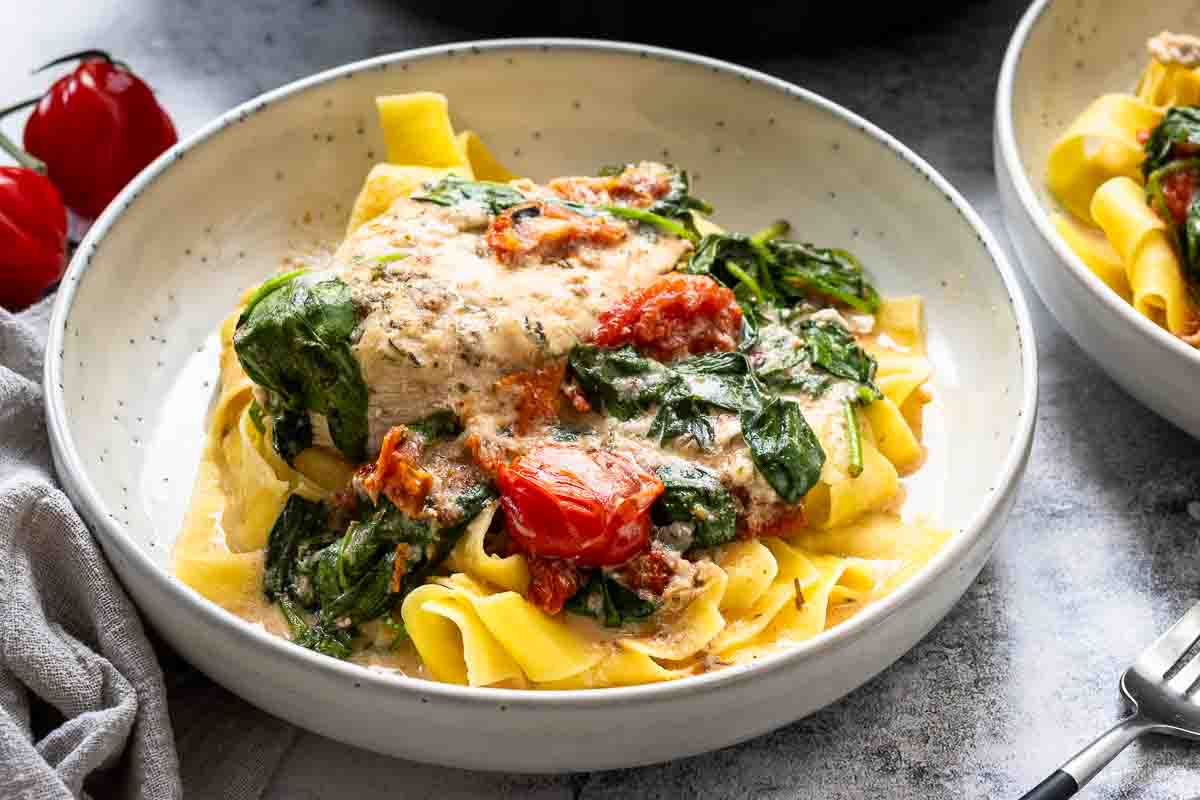 Hähnchenpfanne mit Kokosmilch, Tomaten und Spinat serviert mit Nudeln