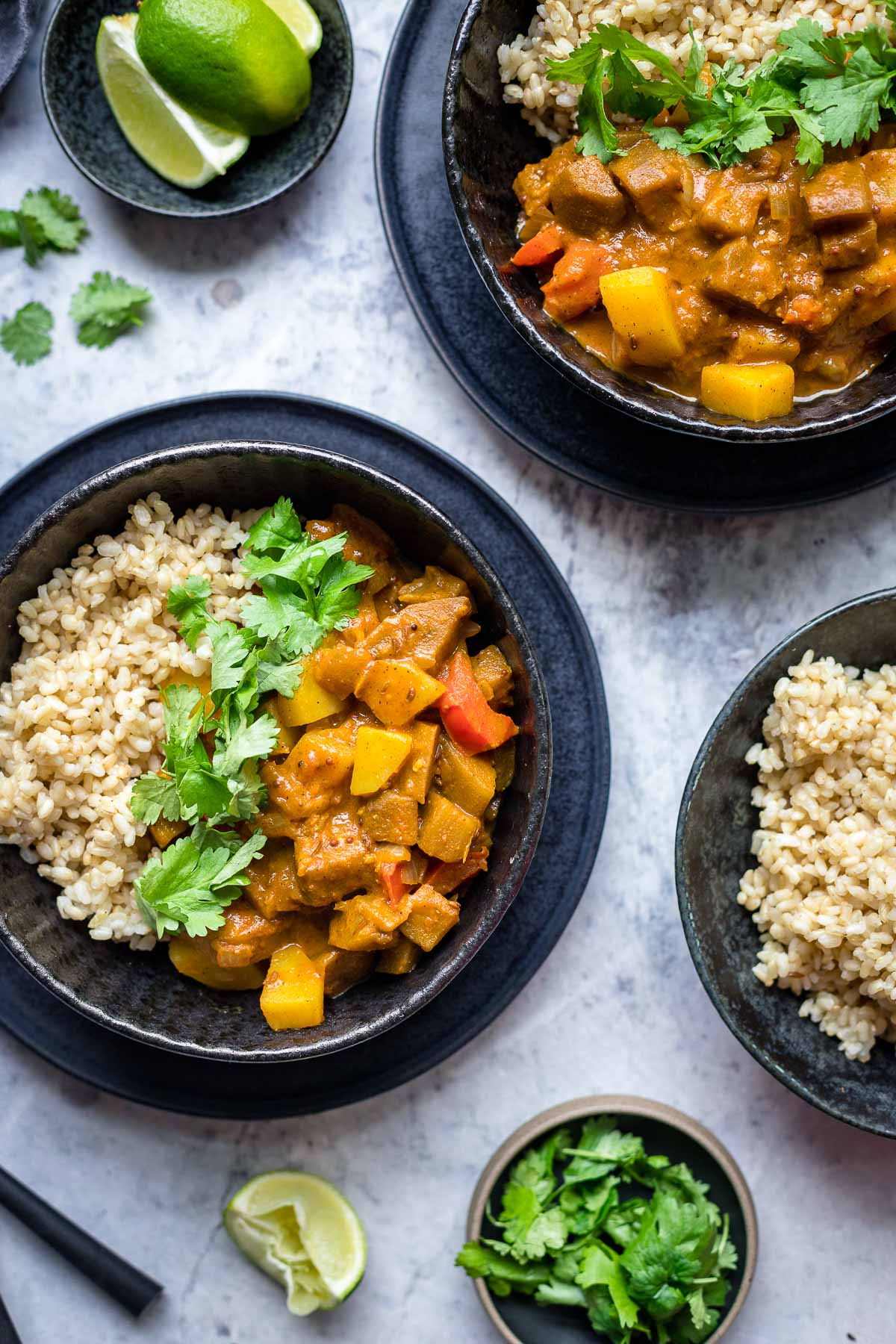 Indisches Auberginen Kartoffel Curry mit Tomaten und Kokosmilch Rezept, serviert mit Vollkornreis, Koriander und Limetten