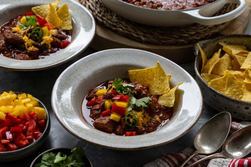 Chili con Carne mit Rindfleisch Rezept serviert mit Paprika, Cheddar-Käse und Tortilla Chips