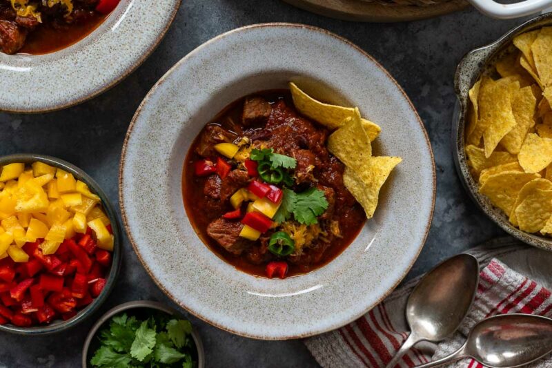 Chili con Carne mit Rindfleisch Rezept serviert mit Paprika, Cheddar-Käse und Tortilla Chips