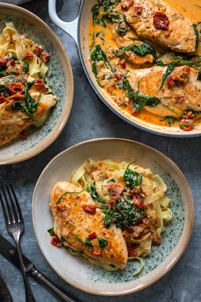 Hähnchen mit Parmesan-Sahnesoße, getrockneten Tomaten und Spinat, serviert über Bandnudeln – ein cremiges und aromatisches Gericht.