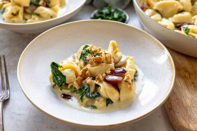 Tortellini in Gorgonzola Sahne Sauce mit Spinat und rote Trauben serviert auf Tellern