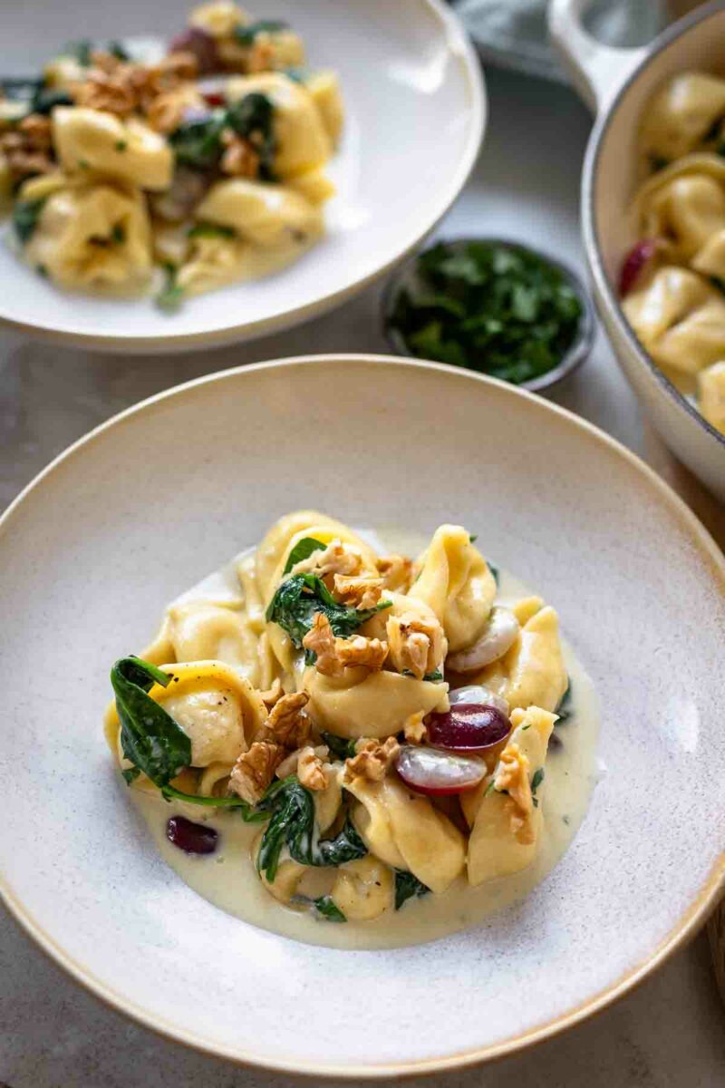 Tortellini in Gorgonzola Sahne Sauce mit Spinat und rote Trauben serviert auf Tellern