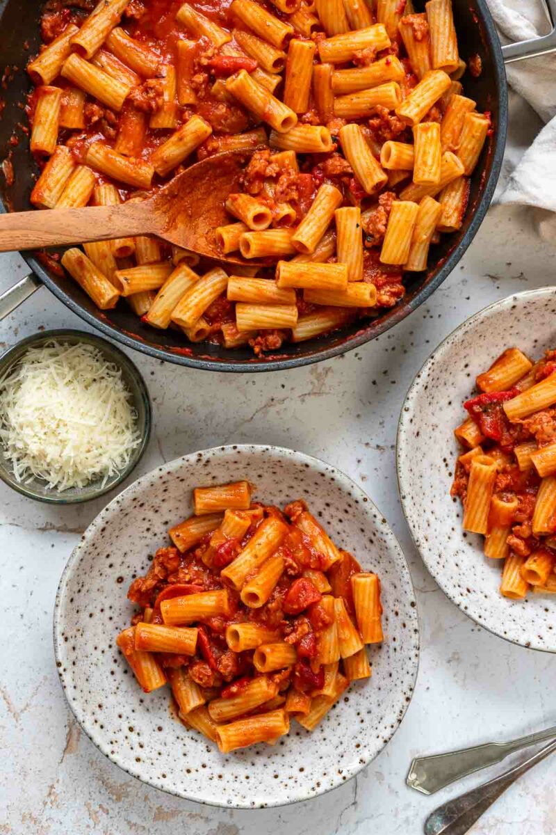 Servierte Pasta mit Salsiccia in pikante Tomaten-Paprika-Sauce, garniert mit Parmesan angerichtet in einer Schüssel.